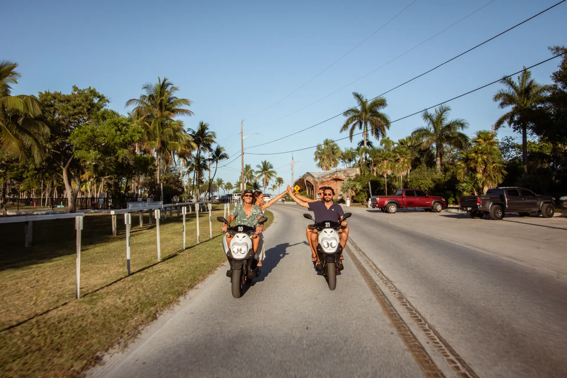 Two couples high-fiving while riding scooters through Key West